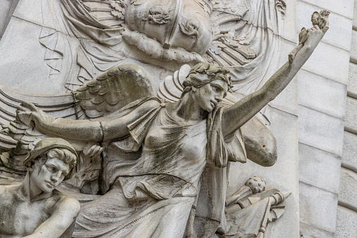 “Spirit of Commerce” is a high relief allegorical sculpture on the north side of the triumphal arch on the Manhattan side of the Manhattan Bridge. The figures are all larger than life. Industry is represented by a dynamically gesturing winged female figure. A male figure in a helmet holding a heavy tool crouches on her on her right, and a female (not seen here) holding a large gear is on her left. 

The sculptor was  Carl Augustus Heber (1871-1956,) and the work was completed in 1914. 

Heber’s model for “Industry” was Audrey Munson.  Munson posed for more than a dozen important statues, sculptures, and friezes, most of which still stand to this day across Manhattan and Brooklyn. She is now often called “America’s First Supermodel.”