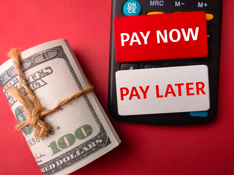 Banknotes and calculator with word PAY NOW PAY LATER on a red background