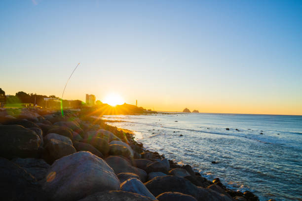 New Plymouth New Zealand - February 28 2024; waterfront view along coast to setting sun and New Plymouth power station chimney.