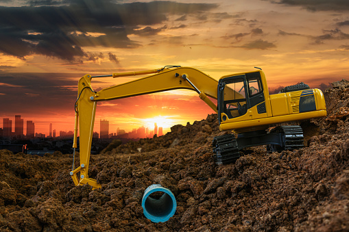 Excavator is digging in the construction site pipeline work on sunset sky at cityscapes background