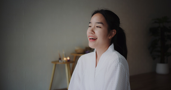 Portrait young woman in bathrobe sits and breathes in fragrance of the air, stretch her arms to relieve fatigue. Gently massage her neck to relax in wellness spa resort, copy space