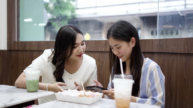 Two young asian women friends sitting at coffee shop having a coffee and chatting with smiling laugh and happiness moment. Female friends meeting at cafe on a weekend, positive attitude relationship