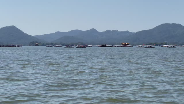 View of tour boats and rowing boats crossing the beautiful West Lake and its mountains of Hangzhou, Zhejiang, China