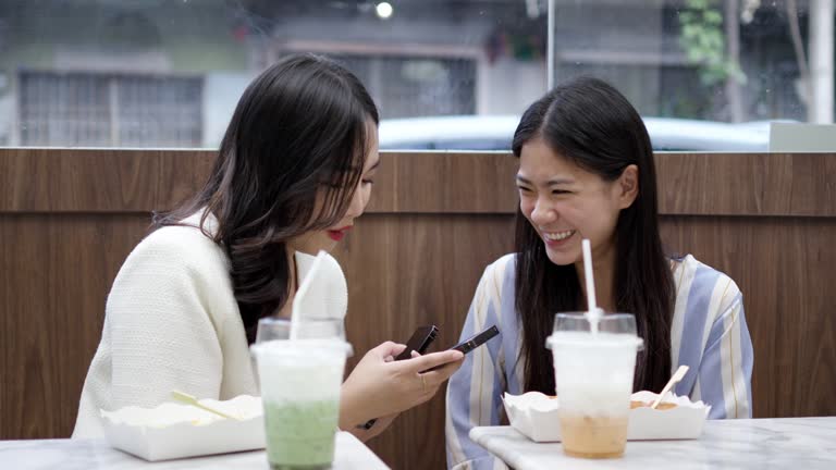 Two young asian women friends sitting at coffee shop having a coffee and chatting with smiling laugh and happiness moment. Female friends meeting at cafe on a weekend, positive attitude relationship