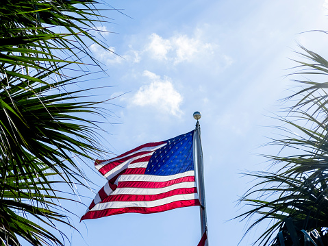 Waving American flag at flagpole over sunny blue sky