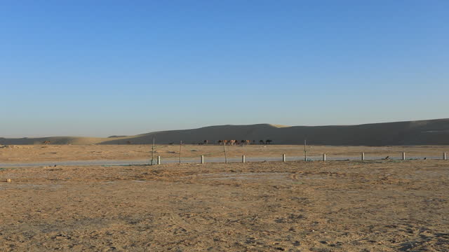 Dry Tunisian desert landscape with clear skies and distant hills, fence in foreground