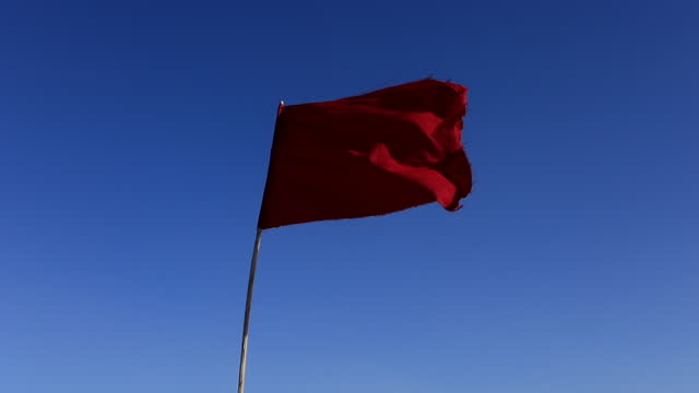 Red flag fluttering against clear blue sky in Tunisian salt desert, Chott el Jerid, symbol of caution