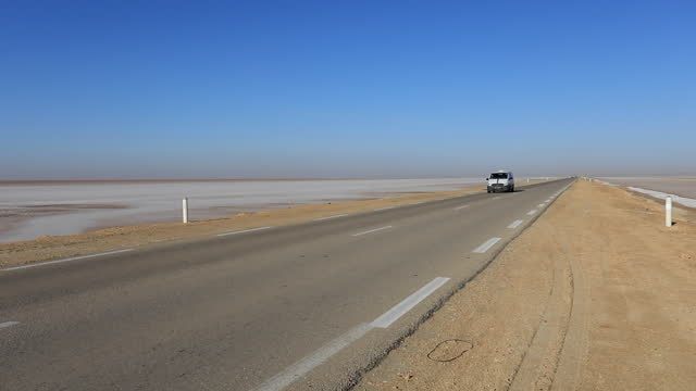 Empty desert road stretching into horizon under clear blue sky, Tunisia