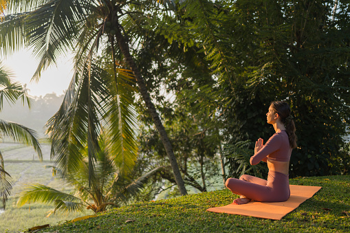 Young woman preforms yoga in tropical rainforest in morning light