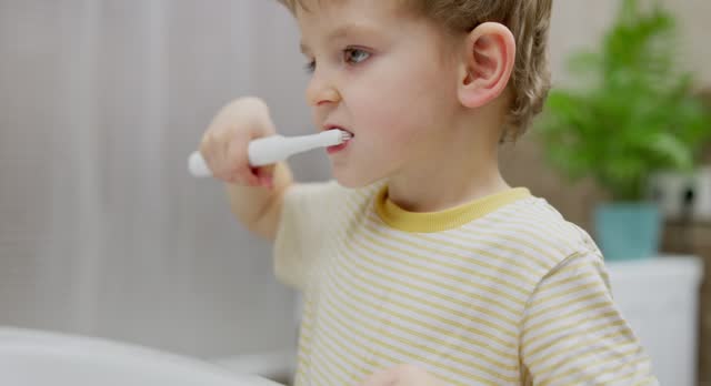 Young child brushing teeth with electric toothbrush in bathroom.