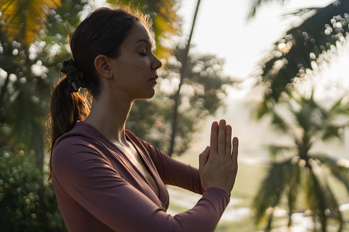Close-up of young woman preforming yoga in tropical rainforest in morning light