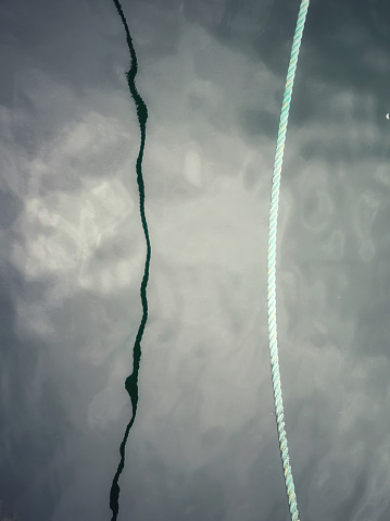 A rope that’s holding the boat in the harbour reflecting on the surface of the water.