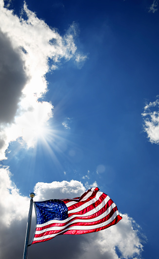 Waving American flag at flagpole over sunny blue sky and shinning sun