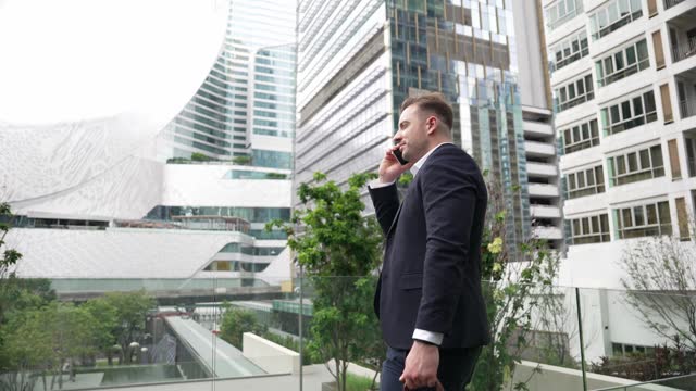 Businessman talking to team by using phone while standing at skyscraper. Urbane.