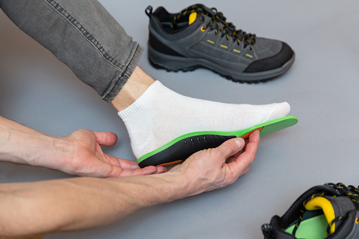 Close up of man hands fitting orthopedic insoles on a gray background. Healthcare and orthopedic treatment and prevention of flatfeet concept.