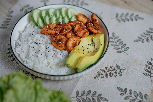 Shrimp Poke Bowl With Avocado and Cucumber served in white plate with floral napkin and wooden spoon and fork for lunch. selective focus. dish for breakfast, lunch and dinner