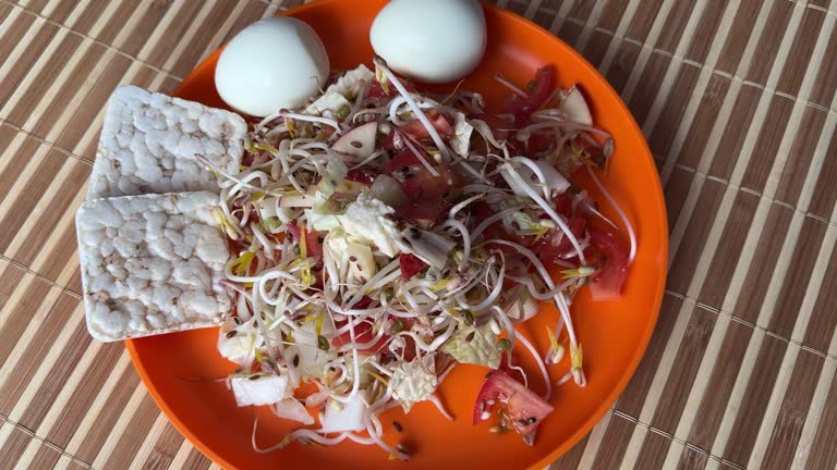 A fresh vegetable salad. Tomatoes, eggs, bread rolls, onions, apples, mound of sprouted mung beans in an orange bowl on bamboo background. Concept of diet, vegan, healthy products. Close up