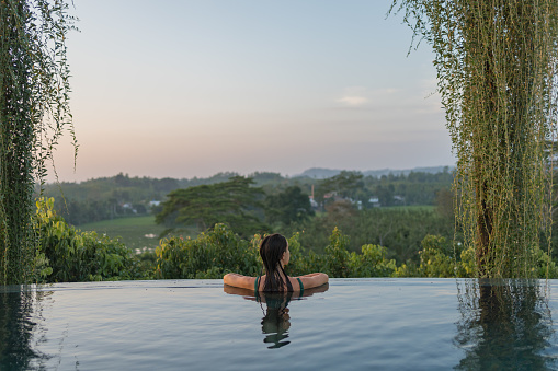 Young woman relaxes on edge of outdoor swimming pool in tropical jungle