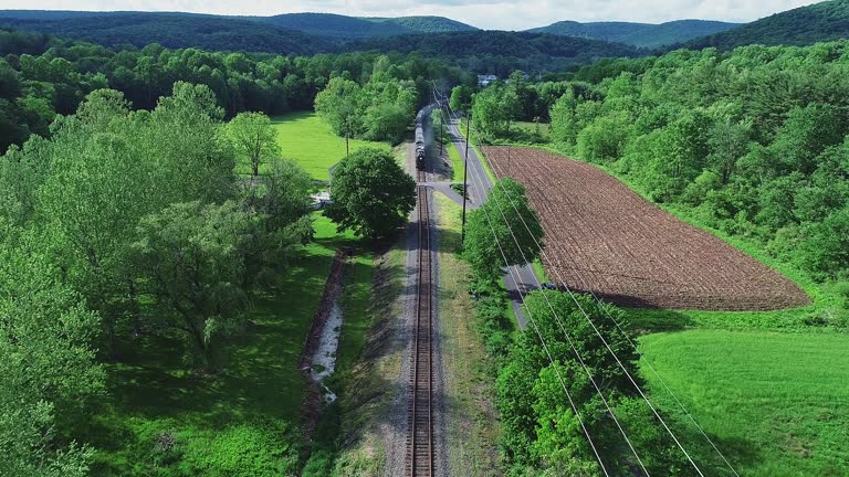 An Aerial View of a Long Steam Passenger Train Approaching on a Single Track Traveling Thru Green Farmlands on a Spring Day