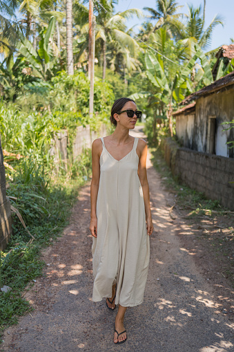 Young woman in sundress walks down pathway in tropical environment