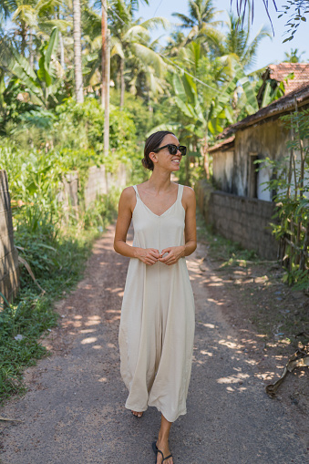 Young woman in sundress walks down pathway in tropical environment