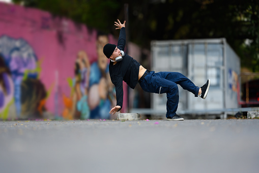 Energetic Asian male dancer stylish clothes dancing hip hop on the street.