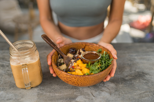 Young woman enjoys vegan salad and iced coffee at outdoor cafe