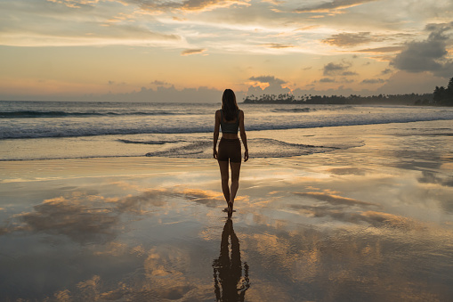 Young woman walks across tidal flats in evening light, reflection in water