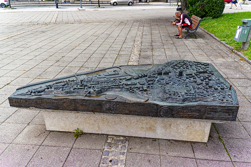 Bronze relief map at Slovenski Square at Slovenian City of Kranj with senior man sitting on bench on a  cloudy summer day. Photo taken August 11th, 2023, Kranj, Slovenia.