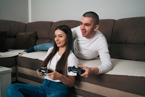 A young couple is sitting on the floor in their cozy home playing video games. The girl is happy because she wins.