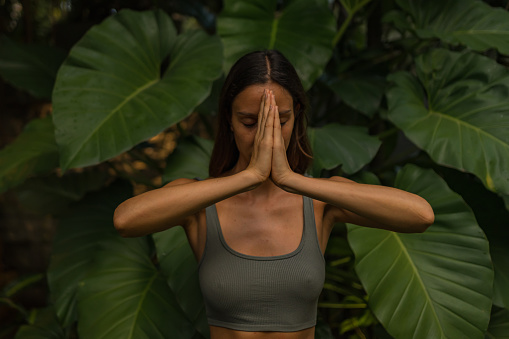 Young woman preforms breathing exercises outdoors in rainforest