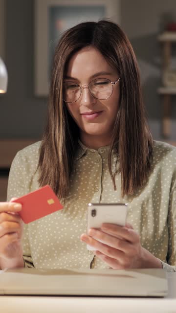 Online shopping. Attractive young friendly woman makes online purchase using her phone and pays with credit card. Close-up