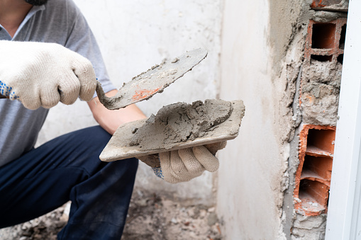 Close-up of a construction worker's hands applying cement with a trowel at a building site, showcasing manual labor and the construction industry in action.