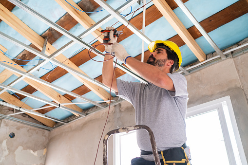 A skilled worker is seen installing the metal framework for a ceiling at a bustling construction site.