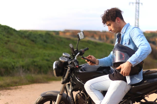 istock Curly haired Caucasian man sitting on his motorcycle using the mobile 2088327744