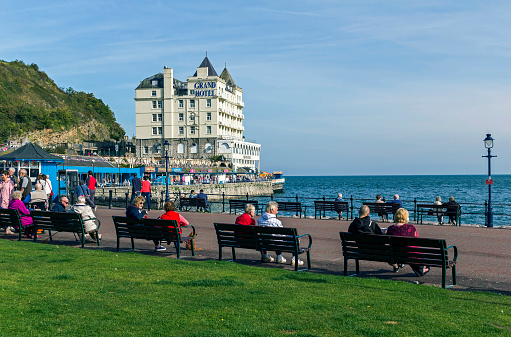 View across the promenade in the centre of Llandudno North Wales UK.  Llandudno pier can be seen in the distance and people can be seen relaxing on the promenade.