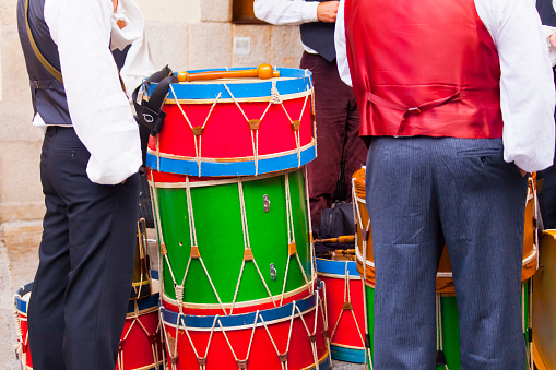 Men wearing historic clothes , stack of  large drums, music band resting. Lugo city, San Froilán, Galicia, Spain.