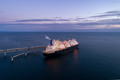 Aerial of Liquified Natural Gas LNG carrier moored to a small gas terminal. Fuel crisis. Sanctions. Wide panoramic shot.