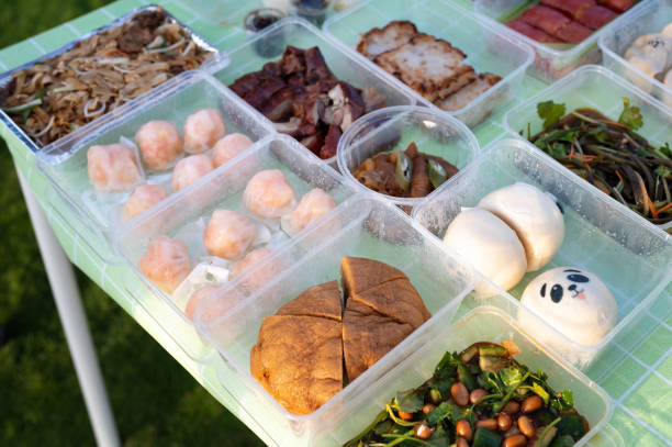 A table is adorned with a full tray of Chinese delicacies ready for picnic, including prepackaged meals, an assortment of vegetables, and various other dishes, making for a delicious and satisfying lunch display. Steamed buns, baozi, roasted duck, cucumber salad and many more