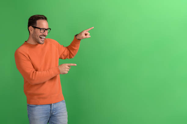 portrait of cheerful salesman pointing at copy space and advertising new product on green background - boegbeeld model stockfoto's en -beelden