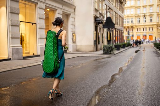 Young woman musician with violin case walking on the street in Vienna.