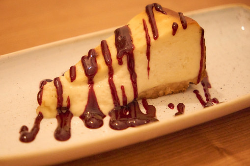 A slice of cheesecake with a chocolate sauce drizzled on top. The sauce is thick and rich, and it contrasts nicely with the creamy texture of the cheesecake. The plate is white