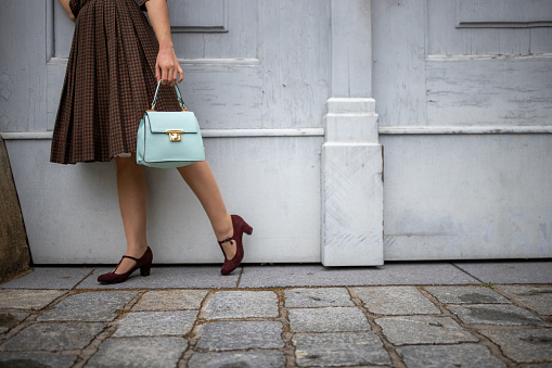 Unrecognizable fashionable young woman holding a purse while standing on the street in Vienna.