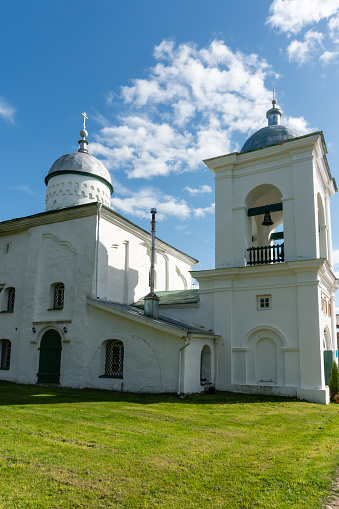 An ancient Russian Orthodox church with thick white stone walls, small windows, a bell tower with bronze bells, domes and crosses, a monument of ancient Russian architecture, history and culture, hiking and tourism, autumn.