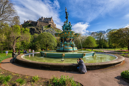 Edinburgh, Scotland, UK - May 9, 2023: Ross Fountain in Princes Street Gardens and Edinburgh Castle on a hill, city landmarks in spring.