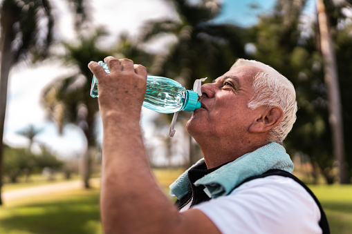 Senior man drinking water after walk at public park