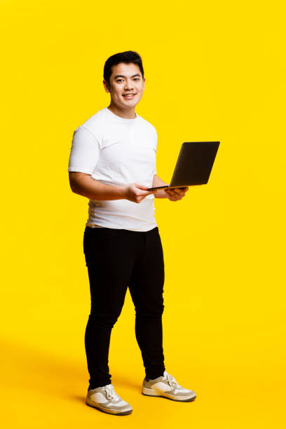 istock Smiling man with laptop on yellow background 2088590934