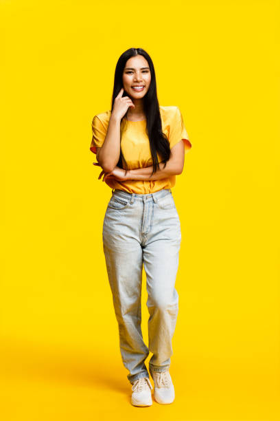 Smiling woman dressed in casual attire poses on a vibrant yellow backdrop