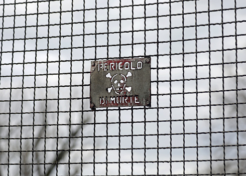 protective metal grille with dark tones and a sign which in Italian means Danger of Death