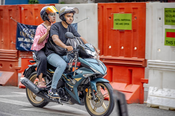 Kuala Lumpur, Malaysia - January 6th 2024: Couple with crash helmets on a motorbike